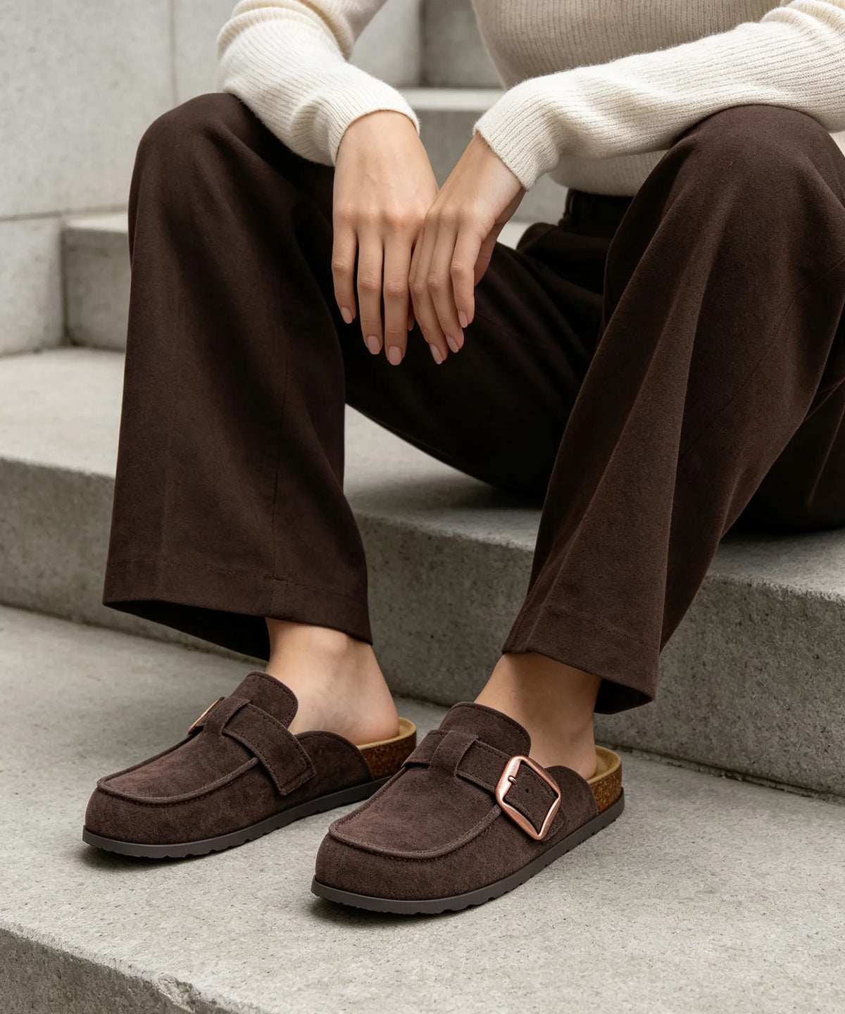 Dark brown slip-on mule clogs worn with brown trousers on steps