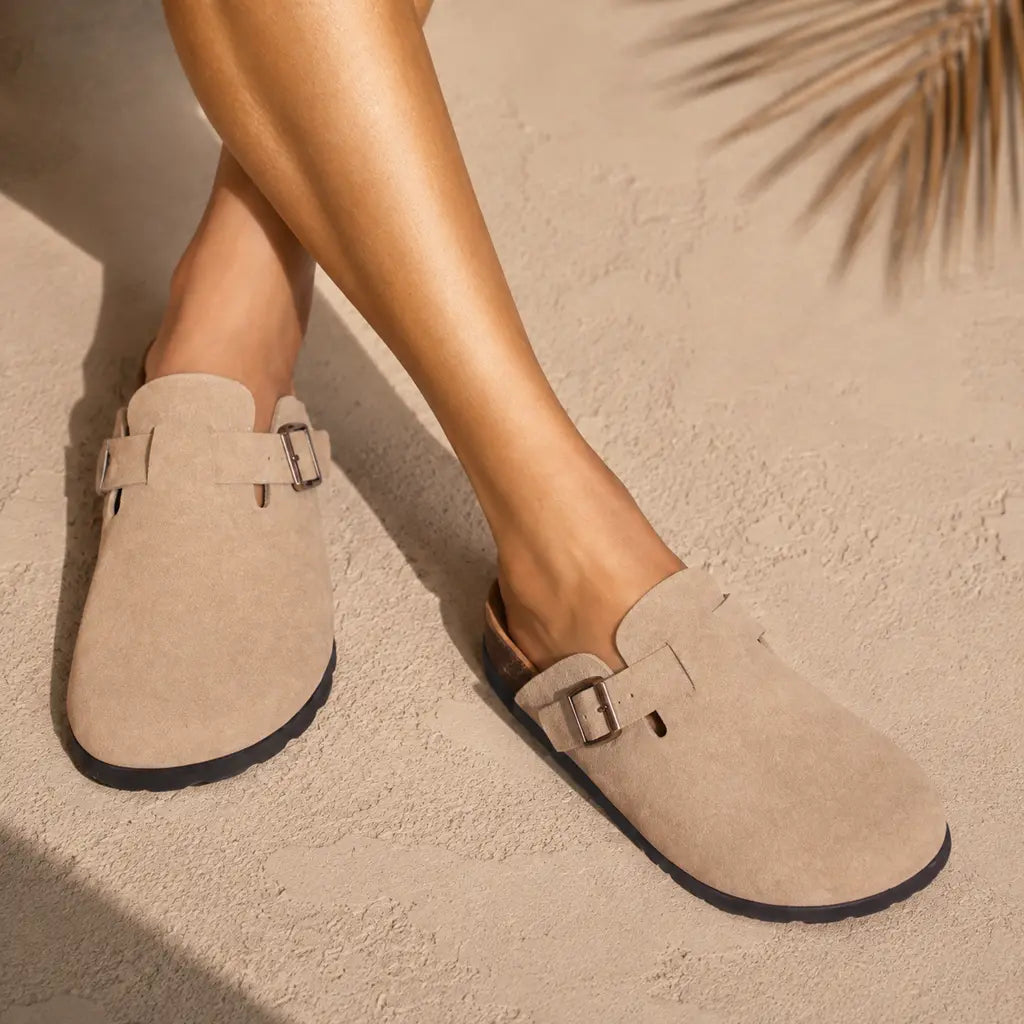 Woman wearing taupe suede buckle clogs with cork footbed on sandy background